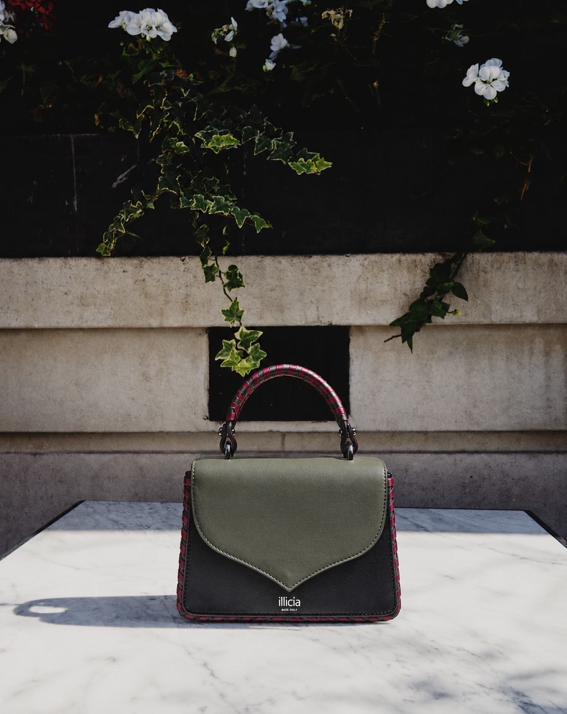 ILLICIA London Celina 2.0 Kale Green and Black leather top handle handbag made in Italy displayed on a marble table