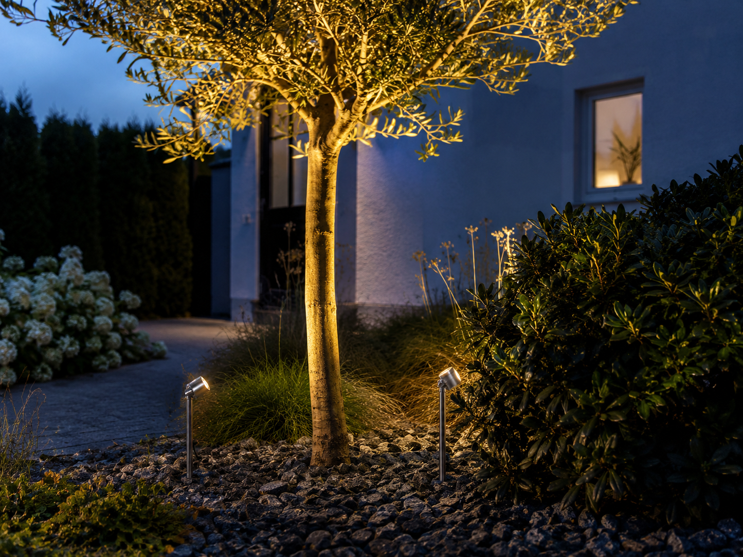 Konstsmide Monza LED garden spot lights illuminating a feature tree in a landscaped garden with warm white 3000K lighting, ideal for pathways, flower beds and modern outdoor spaces.
