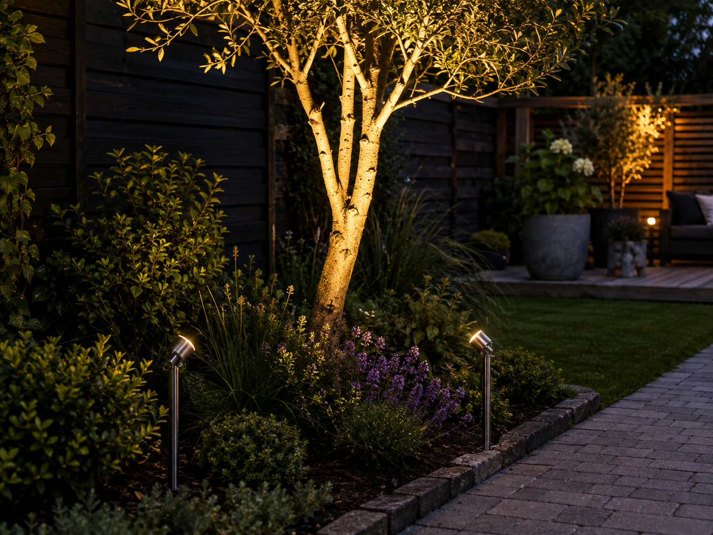 Konstsmide Monza LED garden spot lights highlighting a feature tree with warm white 3000K uplighting in a modern landscaped garden, ideal for outdoor pathways and garden features.