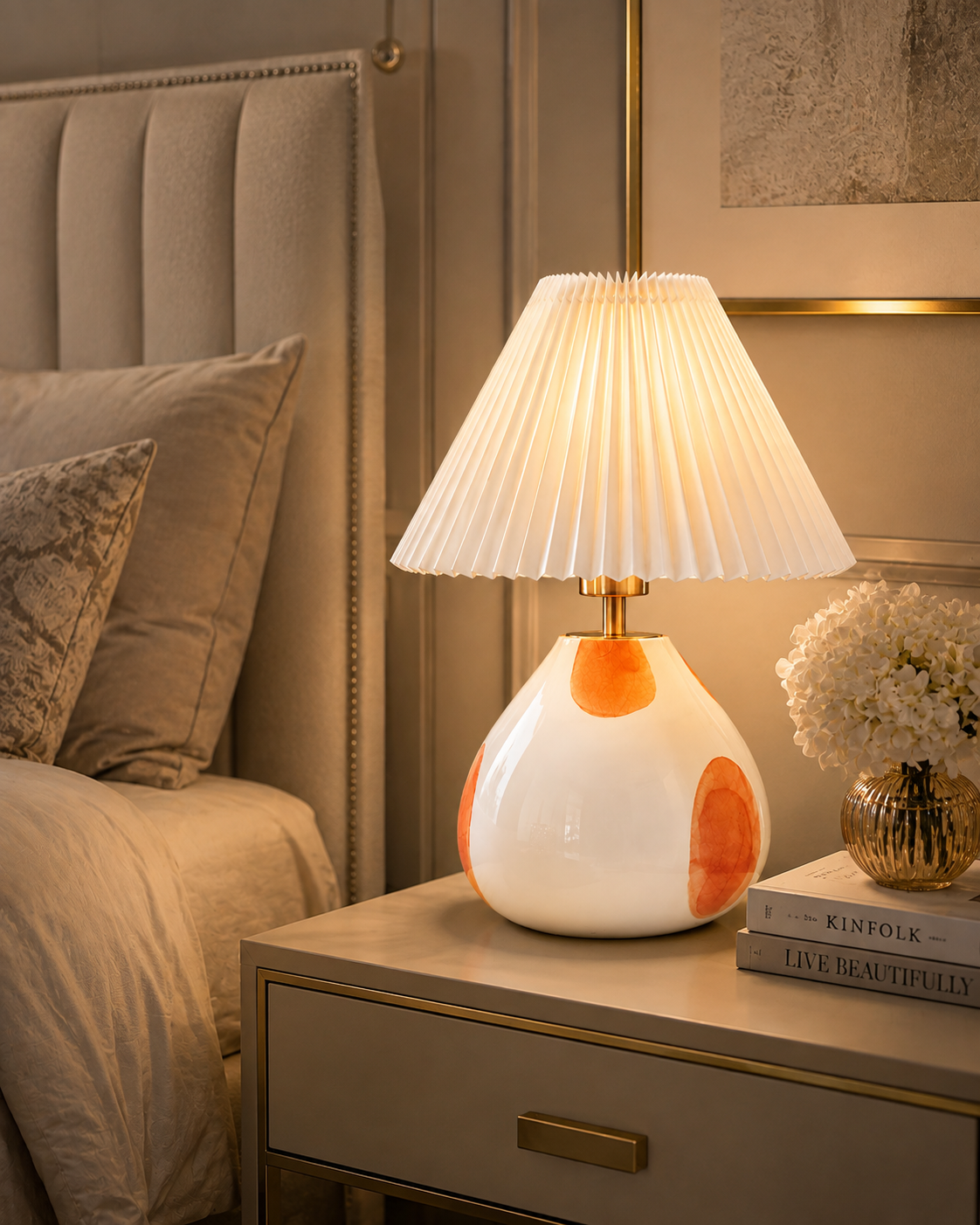 The Very Collection spotted glass table lamp with white pleated shade styled on a bedside table in a modern bedroom, providing warm ambient lighting.